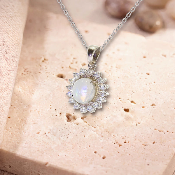 Collier pierre de lune, modèle médaillon ovale bordé de zircons, sur sa chaîne, posé sur une dalle de travertin