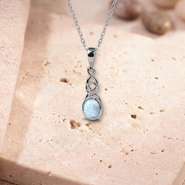 Pendentif argent pierre de lune, modèle ovale sous un entrelacs celtique, sur sa chaîne, posé sur une dalle de travertin