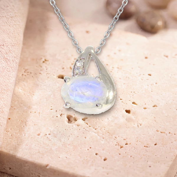Collier pierre de lune femme, modèle ovale facetté sur griffes, sur sa chaîne, posé sur une dalle de travertin