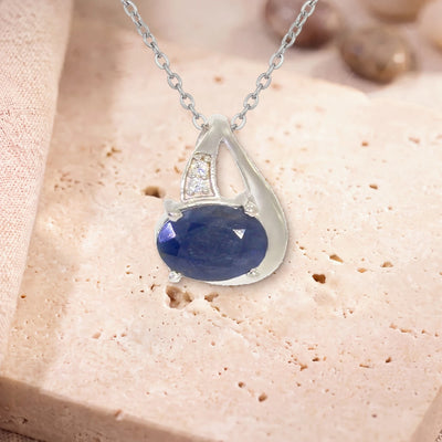 Pendentif saphir argent, modèle ovale facetté sur griffes, sur sa chaîne, posé sur une dalle de travertin