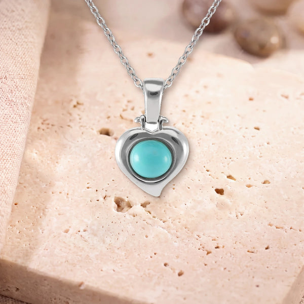 Collier pierre turquoise, modèle en cœur d'argent, sur sa chaîne, posé sur une dalle de travertin
