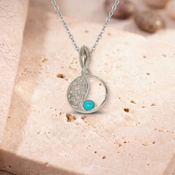 Pendentif pierre turquoise, modèle médaillon ajouré vintage, sur sa chaîne, posé sur une dalle de travertin