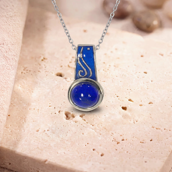 Pendentif pierre lapis lazuli, modèle rond à bélière émaillée, sur sa chaîne, posé sur une dalle de travertin