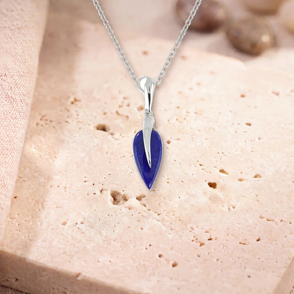 Collier lapis lazuli, modèle grande goutte sous une flamme d'argent, sur sa chaîne, posé sur une dalle de travertin