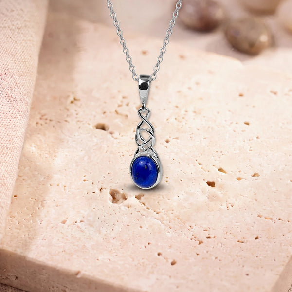 Pendentif lapis lazuli véritable, modèle ovale sous un entrelacs celtique, sur sa chaîne, posé sur une dalle de travertin