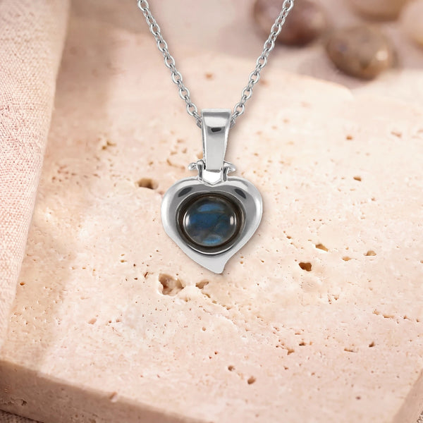 Pendentif labradorite bleue, modèle en cœur d'argent, sur sa chaîne, posé sur une dalle de travertin