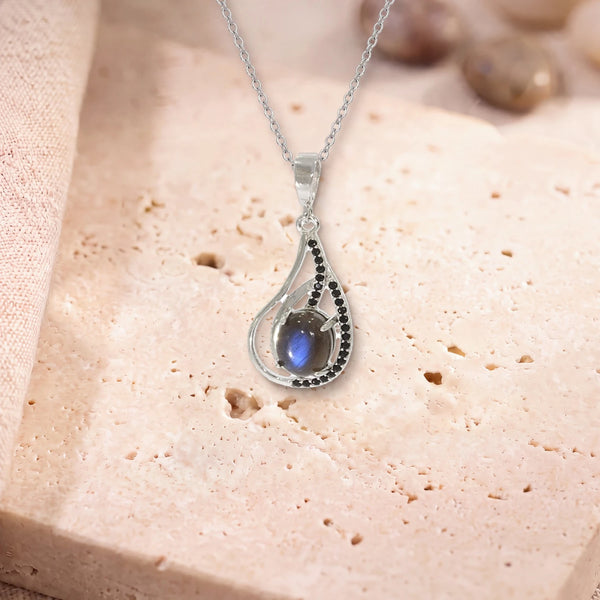 Collier labradorite argent, modèle ovale dans une goutte d'argent ajourée, sur sa chaîne, posé sur une dalle de travertin