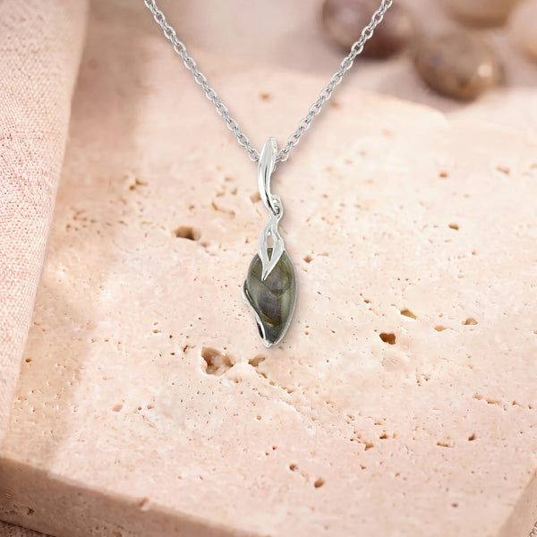 Collier pendentif labradorite, modèle en goutte enlacée d'argent, sur sa chaîne, posé sur une dalle de travertin