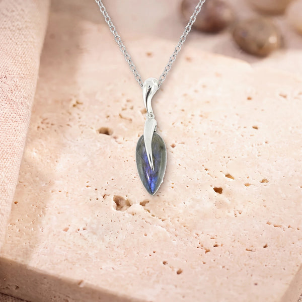 Pendentif labradorite femme, modèle grande goutte sous une flamme d'argent, sur sa chaîne, posé sur une dalle de travertin