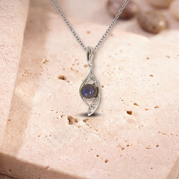 Pendentif labradorite homme, modèle rond dans une navette d'argent ajourée, sur sa chaîne, posé sur une dalle de travertin