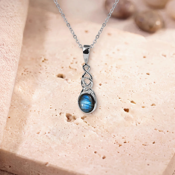 Pendentif labradorite véritable, modèle ovale sous un entrelacs celtique, sur sa chaîne, posé sur une dalle de travertin