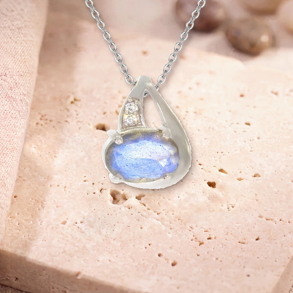 Collier labradorite argent femme, modèle ovale facetté sur griffes, sur sa chaîne, posé sur une dalle de travertin