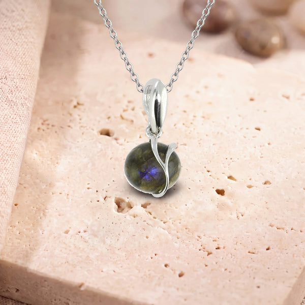 Collier pierre labradorite, modèle rond enlacé d'une liane d'argent, sur sa chaîne, posé sur une dalle de travertin