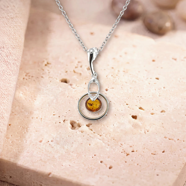 Collier pendentif ambre, modèle rond au centre d'un anneau d'argent, sur sa chaîne, posé sur une dalle de travertin