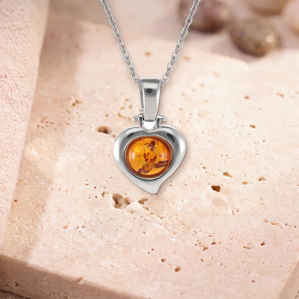Pendentif ambre femme, modèle en cœur d'argent, sur sa chaîne, posé sur une dalle de travertin