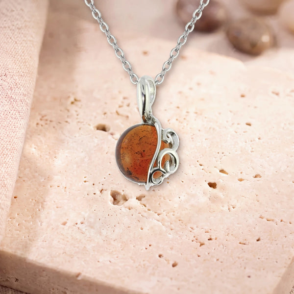 Pendentif ambre homme, modèle grand rond à volutes d'argent, sur sa chaîne, posé sur une dalle de travertin