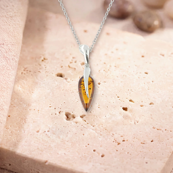 Collier ambre femme, modèle grande goutte sous une flamme d'argent, sur sa chaîne, posé sur une dalle de travertin