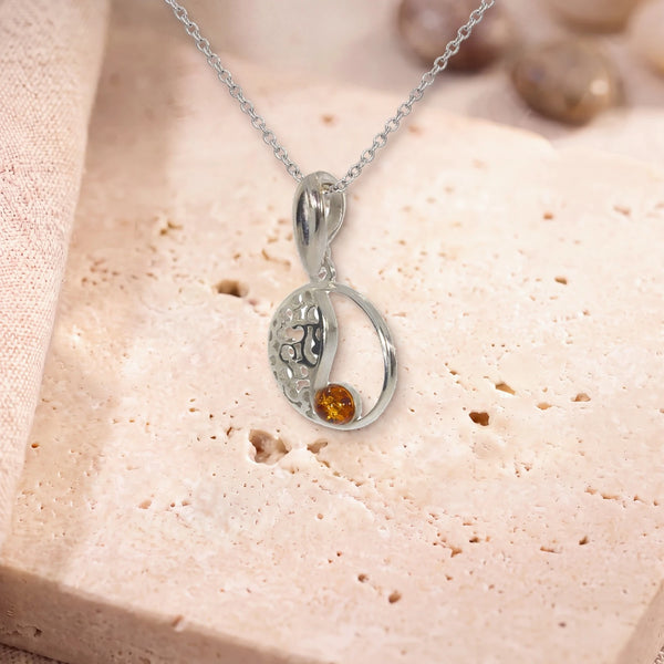 Petit pendentif ambre, modèle médaillon ajouré vintage, sur sa chaîne, posé sur une dalle de travertin