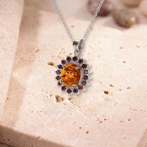 Pendentif pierre d'ambre, modèle médaillon ovale bordé de zircons, sur sa chaîne, posé sur une dalle de travertin