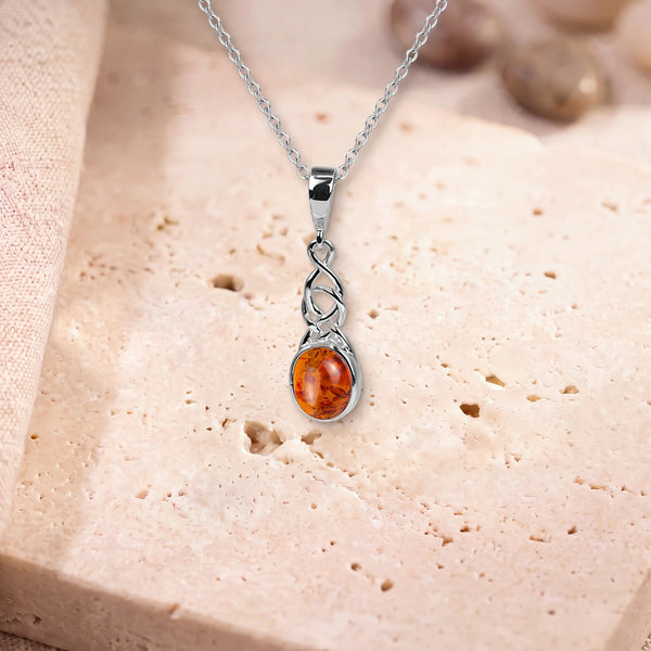 Collier ambre et argent, modèle ovale sous un entrelacs celtique, sur sa chaîne, posé sur une dalle de travertin
