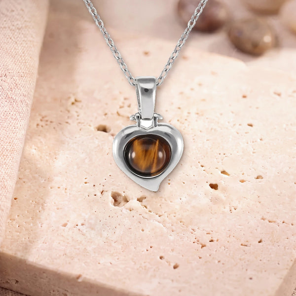 Collier œil de tigre protection, modèle en cœur d'argent, sur sa chaîne, posé sur une dalle de travertin