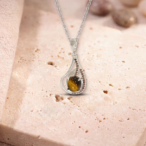 Cadeau pendentif œil de tigre, modèle ovale dans une goutte d'argent ajourée, sur sa chaîne, posé sur une dalle de travertin