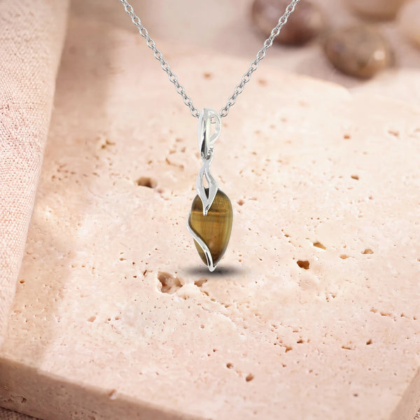 Pendentif œil de tigre naturel, modèle en goutte enlacée d'argent, sur sa chaîne, posé sur une dalle de travertin