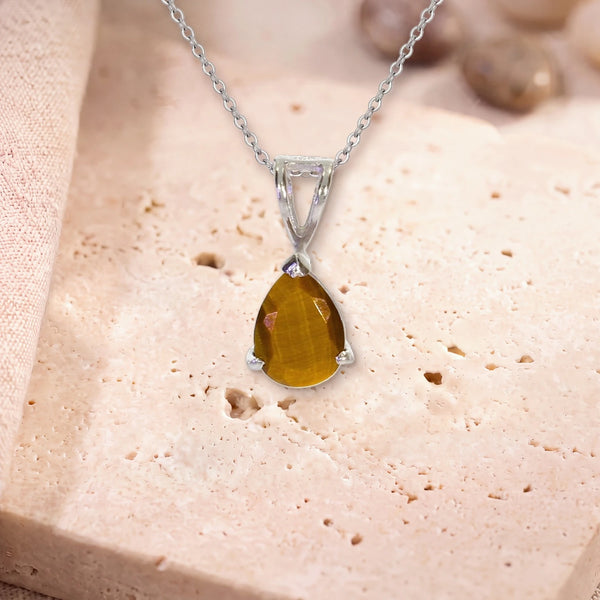 Petit pendentif œil de tigre, modèle petite goutte facettée, sur sa chaîne, posé sur une dalle de travertin