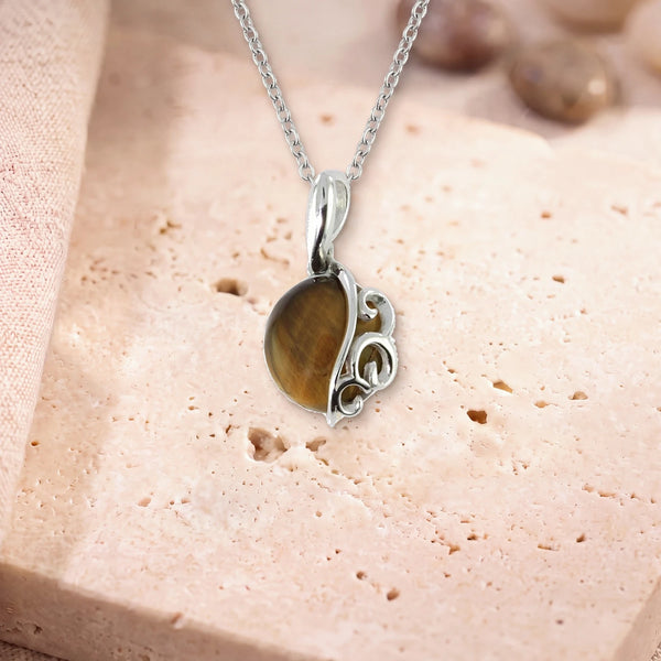 Collier œil de tigre homme, modèle grand rond à volutes d'argent, sur sa chaîne, posé sur une dalle de travertin