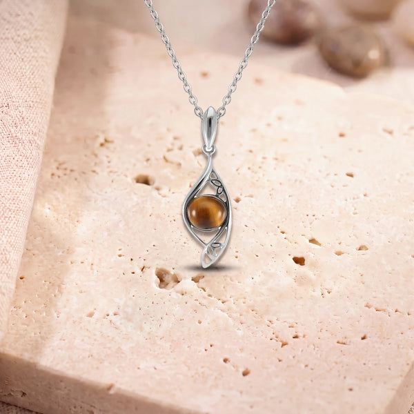 Pendentif œil de tigre homme, modèle rond dans une navette d'argent ajourée, sur sa chaîne, posé sur une dalle de travertin
