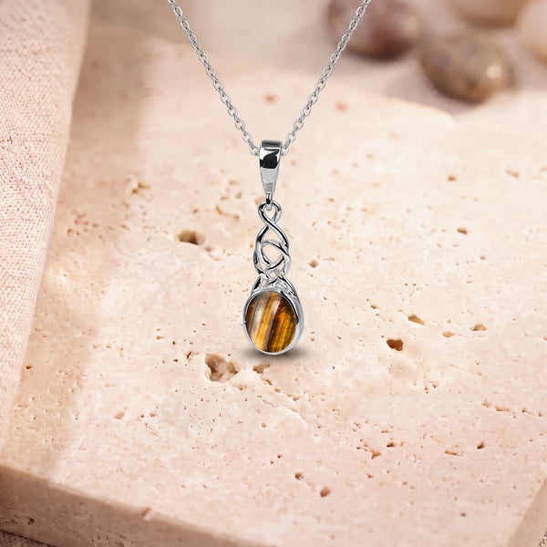 Pendentif œil de tigre femme, modèle ovale sous un entrelacs celtique, sur sa chaîne, posé sur une dalle de travertin