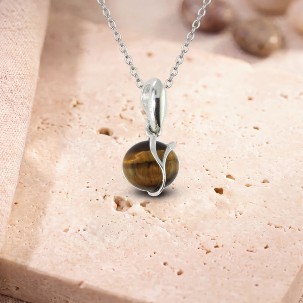 Collier pierre œil de tigre, modèle rond enlacé d'une liane d'argent, sur sa chaîne, posé sur une dalle de travertin