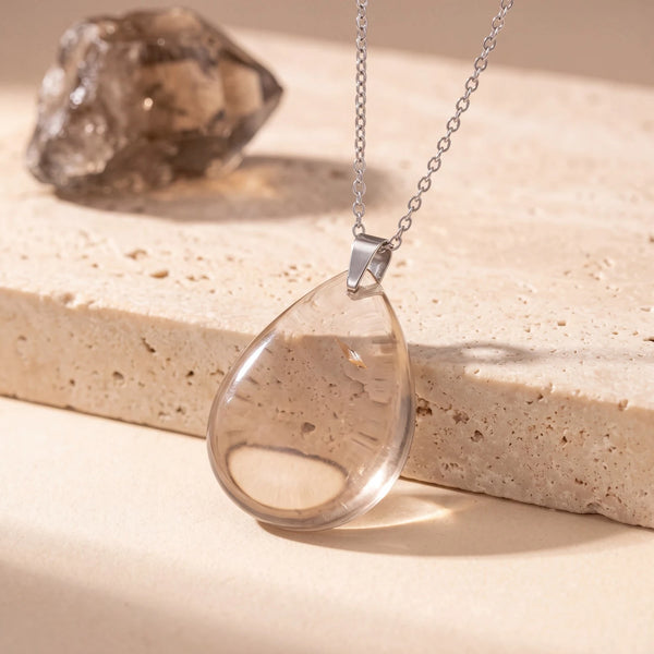 Pendentif pierre marron en quartz fumé, goutte plate translucide sur chaîne argentée, posé sur du travertin