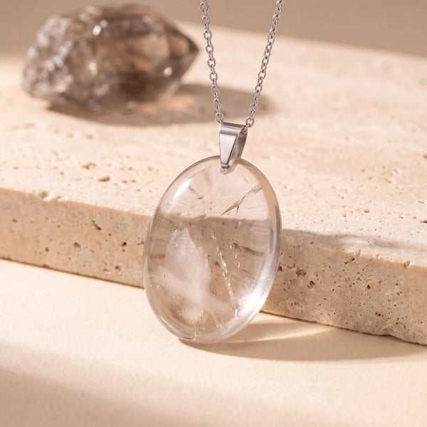 Pendentif pierre marron ovale en quartz fumé, plat et translucide, posé sur une dalle de travertin