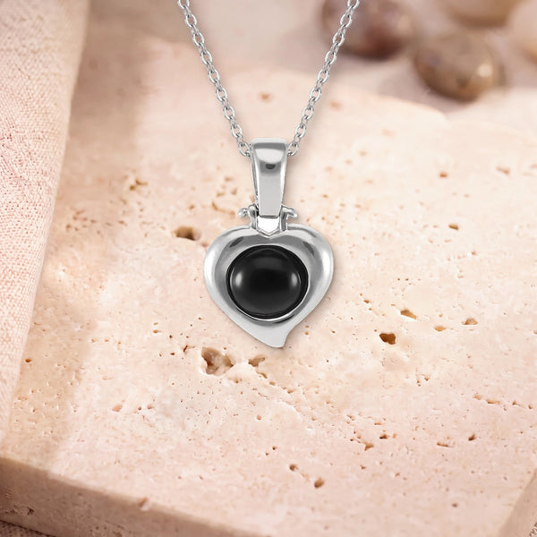Pendentif onyx, modèle en cœur d'argent, sur sa chaîne, posé sur une dalle de travertin