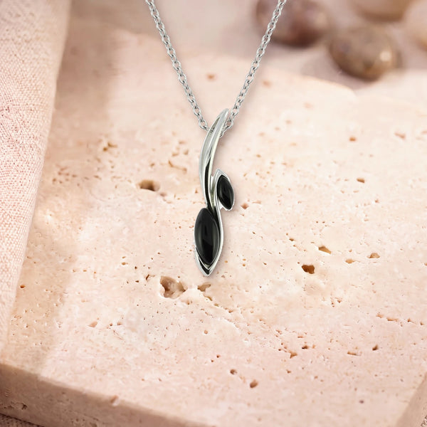 Pendentif pierre noire homme, modèle deux navettes sur une tige d'argent, sur sa chaîne, posé sur une dalle de travertin