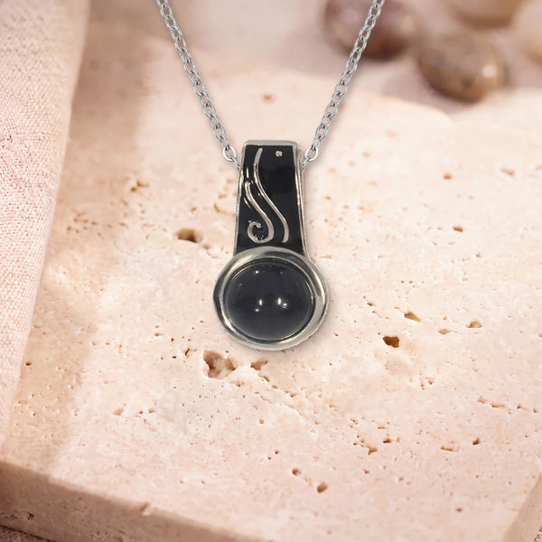 Pendentif pierre onyx, modèle rond à bélière émaillée, sur sa chaîne, posé sur une dalle de travertin