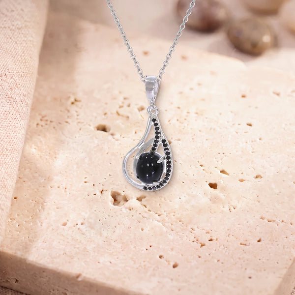 Collier pierre noire femme, modèle ovale dans une goutte d'argent ajourée, sur sa chaîne, posé sur une dalle de travertin
