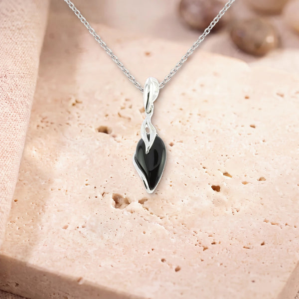 Pendentif onyx goutte, modèle en goutte enlacée d'argent, sur sa chaîne, posé sur une dalle de travertin