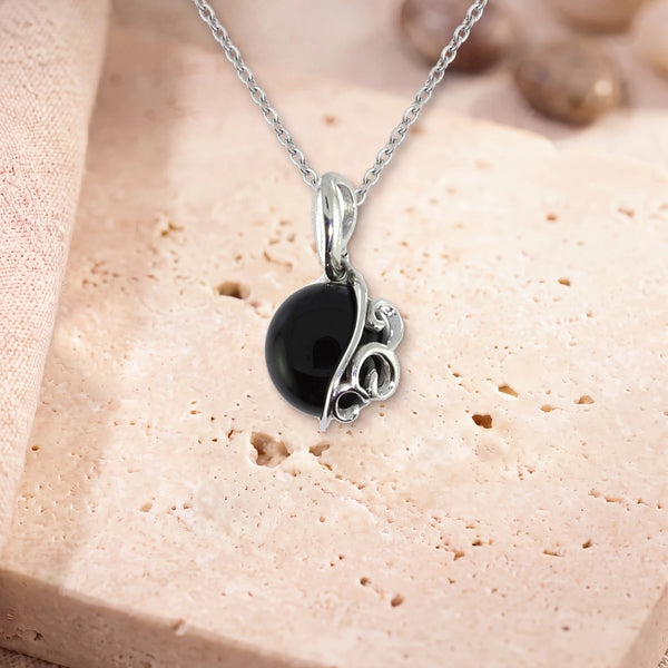 Collier onyx homme, modèle grand rond à volutes d'argent, sur sa chaîne, posé sur une dalle de travertin
