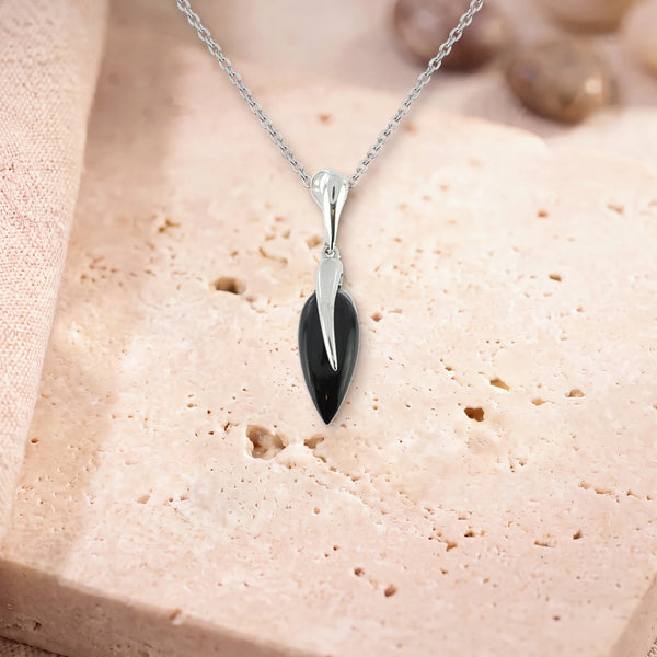 Collier onyx, modèle grande goutte sous une flamme d'argent, sur sa chaîne, posé sur une dalle de travertin