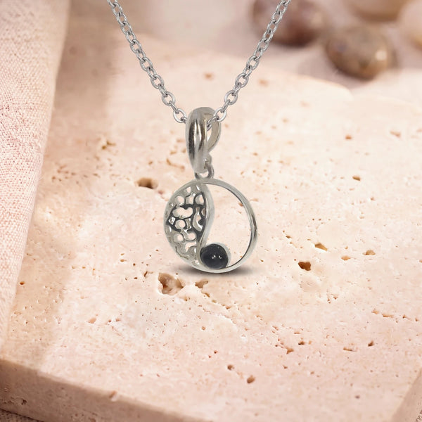 Collier argent onyx, modèle médaillon ajouré vintage, sur sa chaîne, posé sur une dalle de travertin