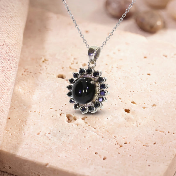 Pendentif onyx noir femme, modèle médaillon ovale bordé de zircons, sur sa chaîne, posé sur une dalle de travertin