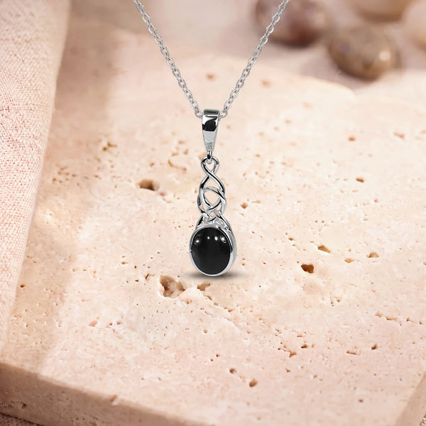 Collier onyx femme, modèle ovale sous un entrelacs celtique, sur sa chaîne, posé sur une dalle de travertin