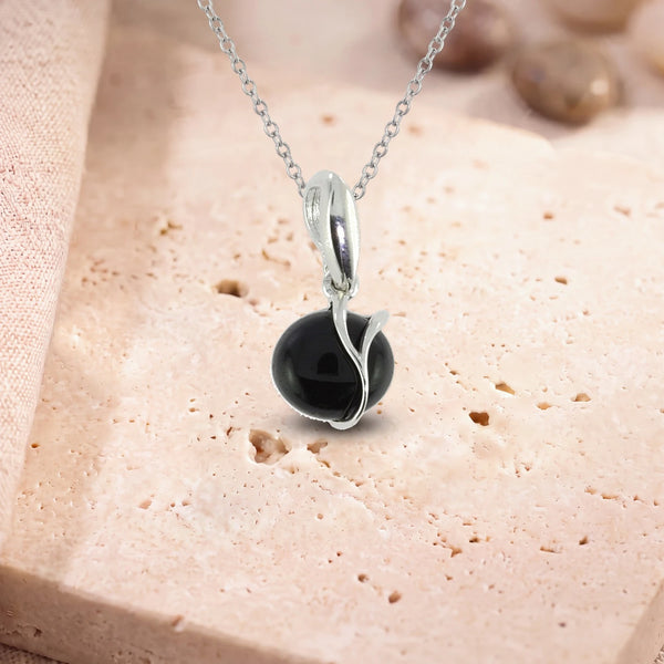 Pendentif onyx noir et argent, modèle rond enlacé d'une liane d'argent, sur sa chaîne, posé sur une dalle de travertin