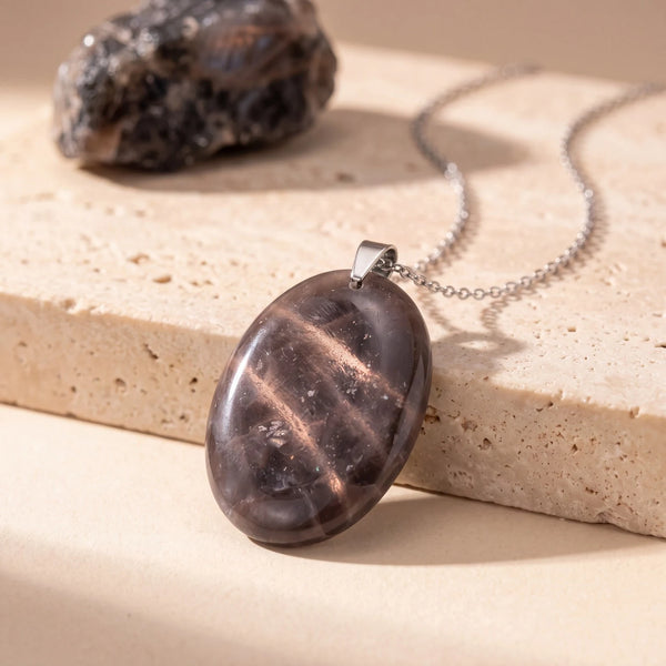 Pendentif pierre noire ovale en pierre de lune, plat et poli aux reflets argentés sur travertin