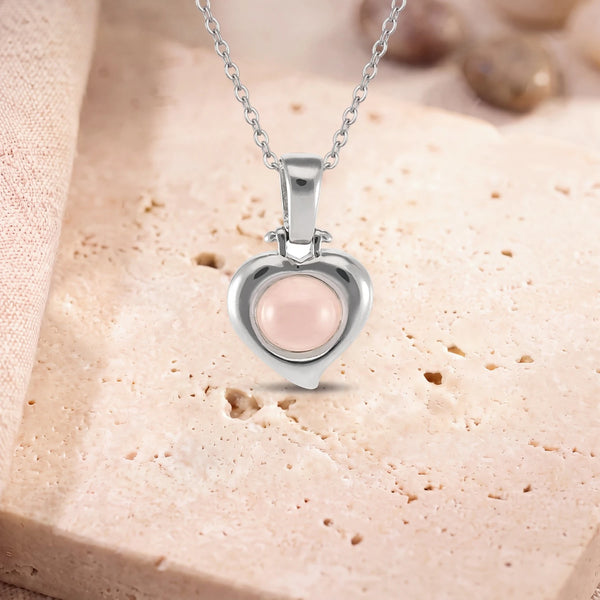 Collier pierre quartz rose, modèle en cœur d'argent, sur sa chaîne, posé sur une dalle de travertin