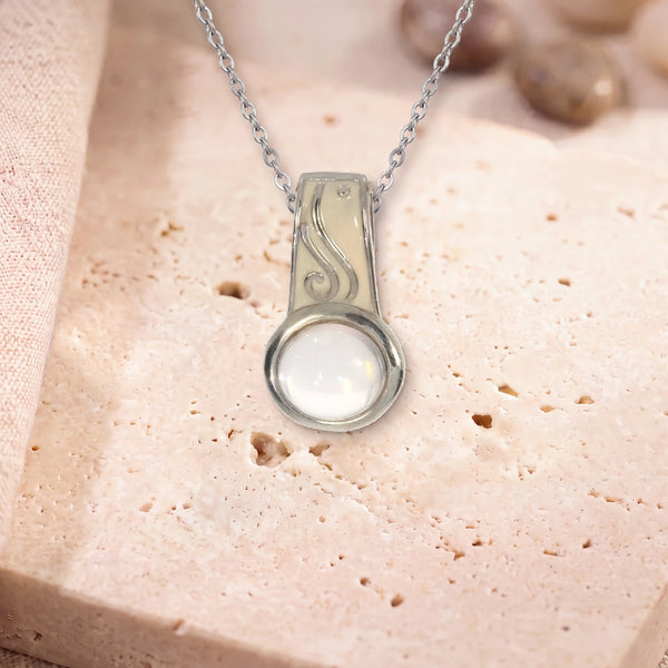 Pendentif quartz rose bohème, modèle rond à bélière émaillée, sur sa chaîne, posé sur une dalle de travertin