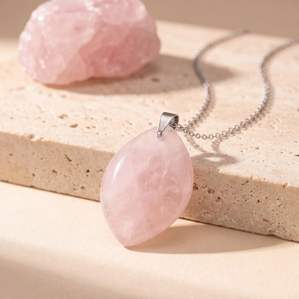 Pendentif pierre rose en quartz rose, forme libre plate polie sur chaîne argentée, posée sur du travertin