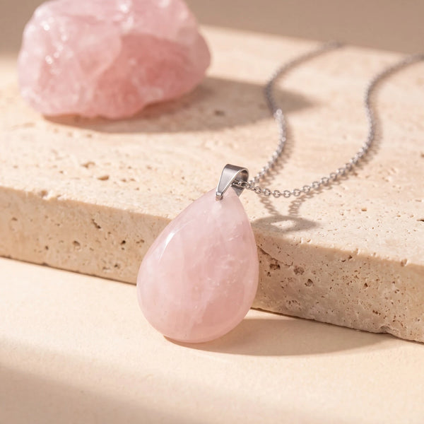 Pendentif pierre rose en quartz rose, goutte plate polie sur chaîne argentée, posée sur une dalle de travertin